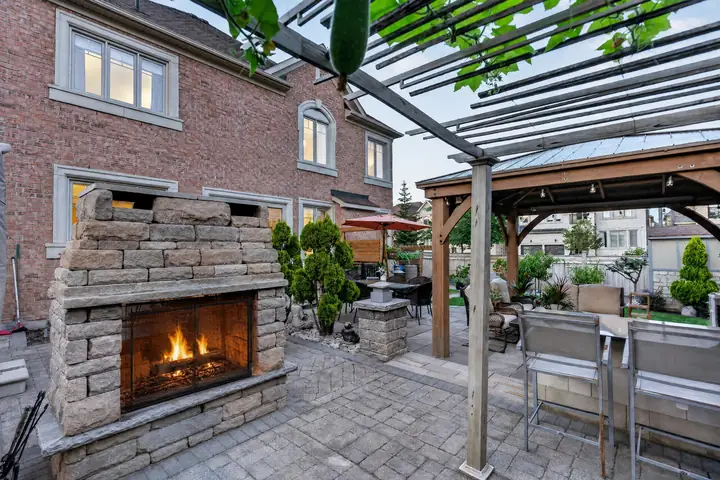 Pergola and stone fireplace beside a brick home